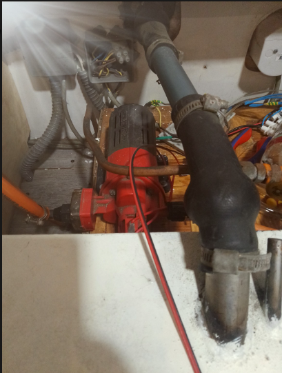 12V RV water pump installed under a camper sink, connected to red and clear hoses
